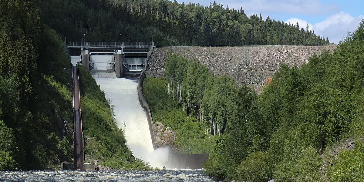Vattenkraftsdamm med utskov omgiven av granskog