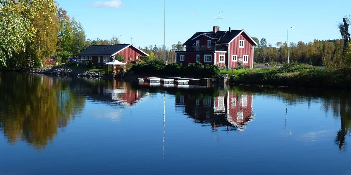 Röda dalastugor vid Lillälven i Torsång speglar sig i stilla vatten