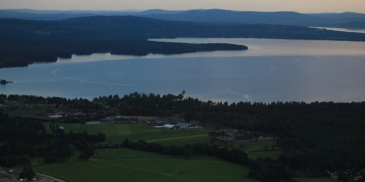 Flygfoto över Rättvik med kyrka, åkrar och Siljan i kvällsljus