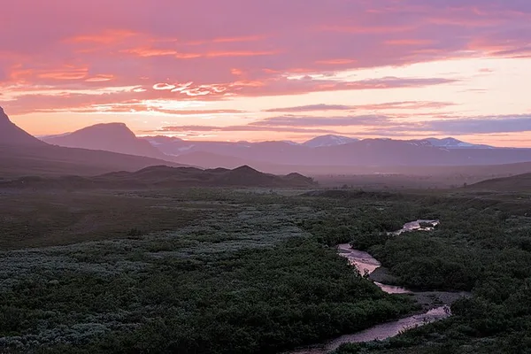 Fjällvy med bäck genom videmark i rosa kvällsljus
