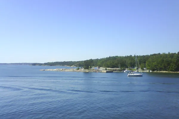 Skärgårdsvy med segelbåt vid klippig kust och barrskog